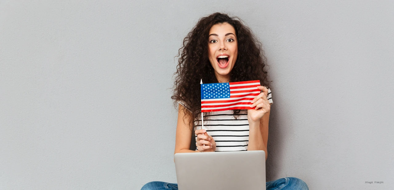 كيفية تعلم الإنجليزية بسرعة، فتاة تحمل العلم الأمريكي وحاسوباً محمولاً