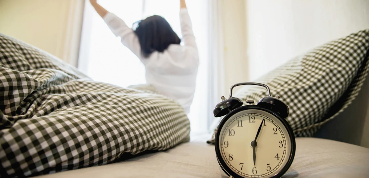 Talking About Your Daily Routine in English for Beginners, a girl waking up in the morning with her alarm clock at 6:05 AM